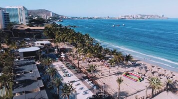 Un hotel frente a la playa con piscina, palmeras y vistas al océano.