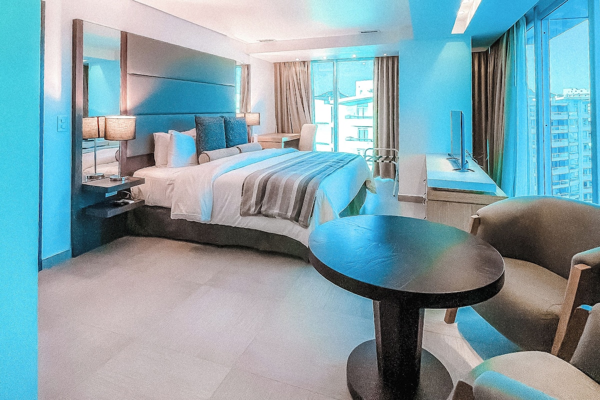 Une chambre d’hôtel moderne avec un lit aux courbes élégantes, une table ronde et une vue sur la ville.