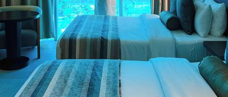 A hotel room with a large window, a bed with striped bedding, a sofa with pillows, and a small table.