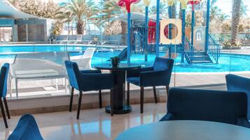 A poolside area with blue chairs and a table, overlooking a swimming pool and palm trees.