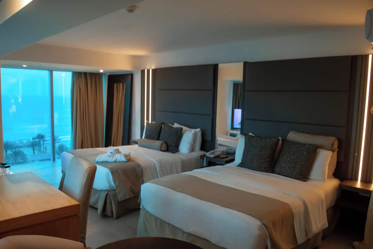 Une chambre d’hôtel avec deux lits, un bureau et une grande fenêtre avec des rideaux.