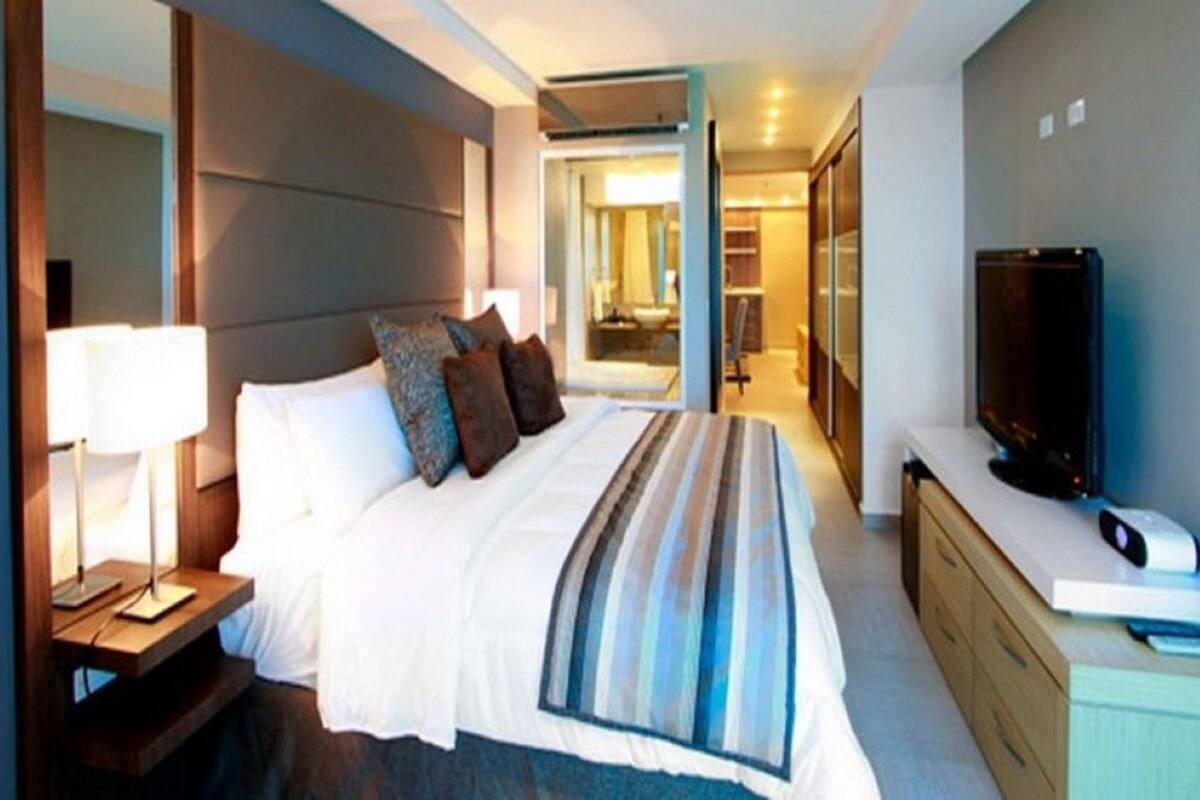 Une chambre d’hôtel moderne dotée d’un grand lit, de lampes de chevet, d’un téléviseur à écran plat et d’un dressing.