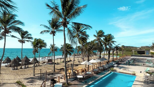 Ein Poolbereich eines Resorts mit freiem Blick auf den Ozean, Palmen und Liegestühle.
