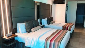 A hotel room with two beds, a bedside table, a nightstand, a mirror, and a built-in air conditioning unit.