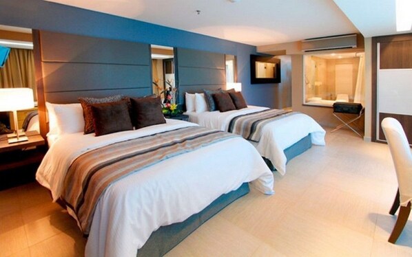 Habitación de hotel con dos camas, un escritorio, una silla y un ventanal grande.