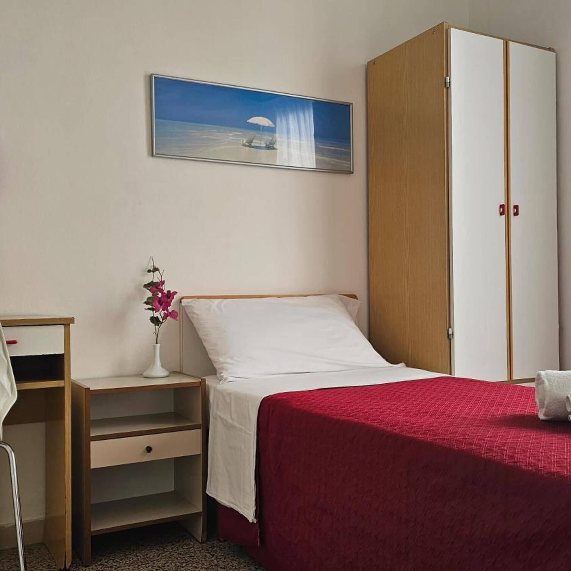 A bedroom with a bed, a nightstand, a desk, a wardrobe, and a painting on the wall.