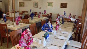 A dining area with multiple tables set for meals, each with floral centerpieces and white napkins. - Hotel Bel Air (Rimini)