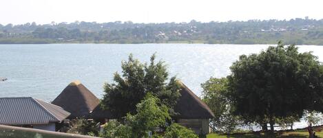 A lakeside view with thatched-roof cottages, a grassy area, and a distant tree line.