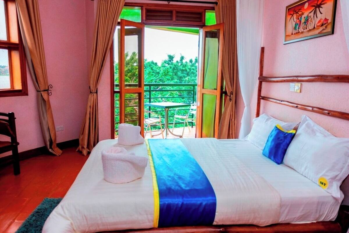 A hotel room with a bed, a chair, a balcony with a table and chairs, and a painting on the wall.