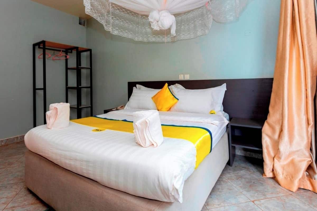 A neatly made bed with white and yellow bedding, a bedside table, and a hanging light fixture.