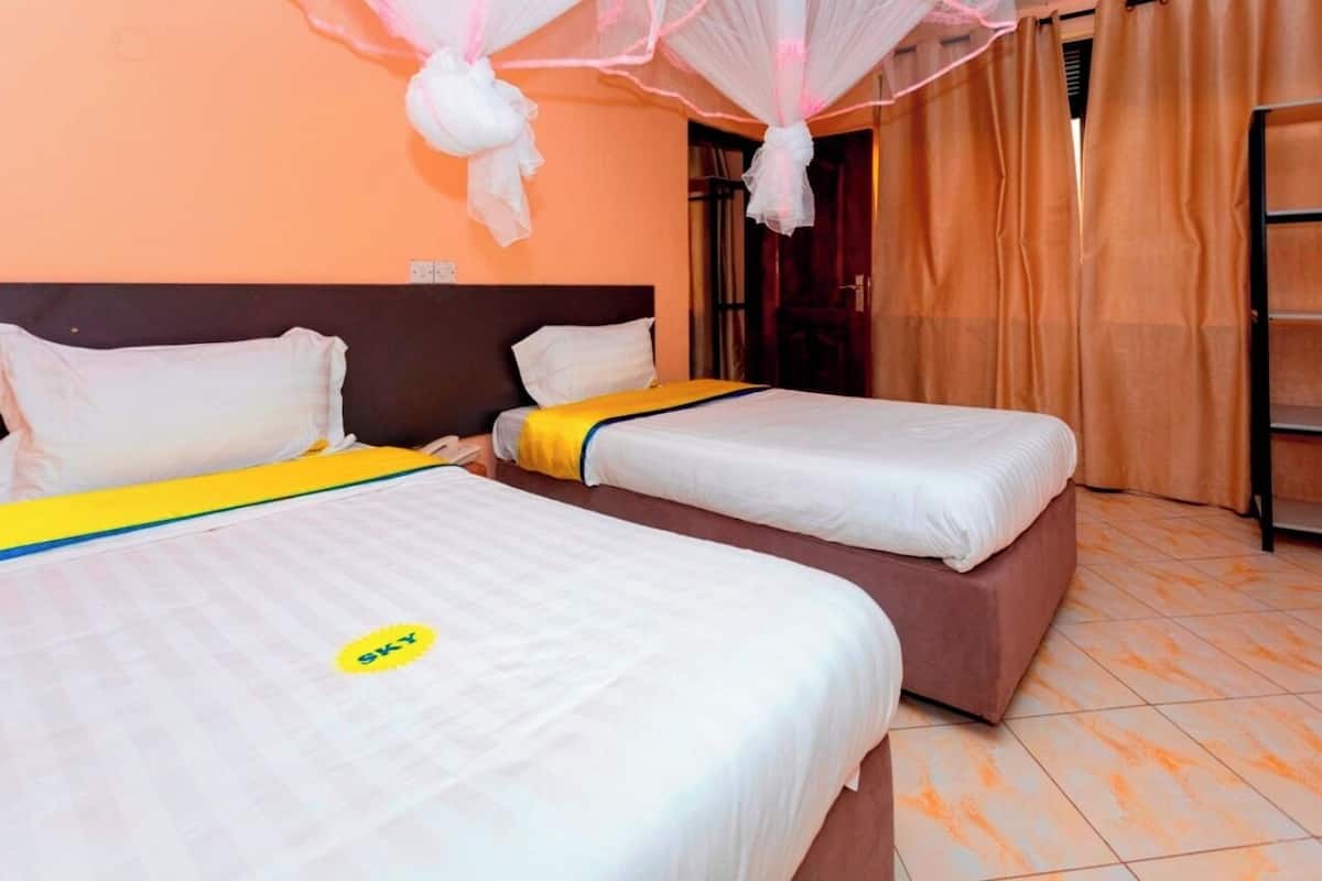 A hotel room with two beds, a headboard, a mosquito net, and a window with curtains.