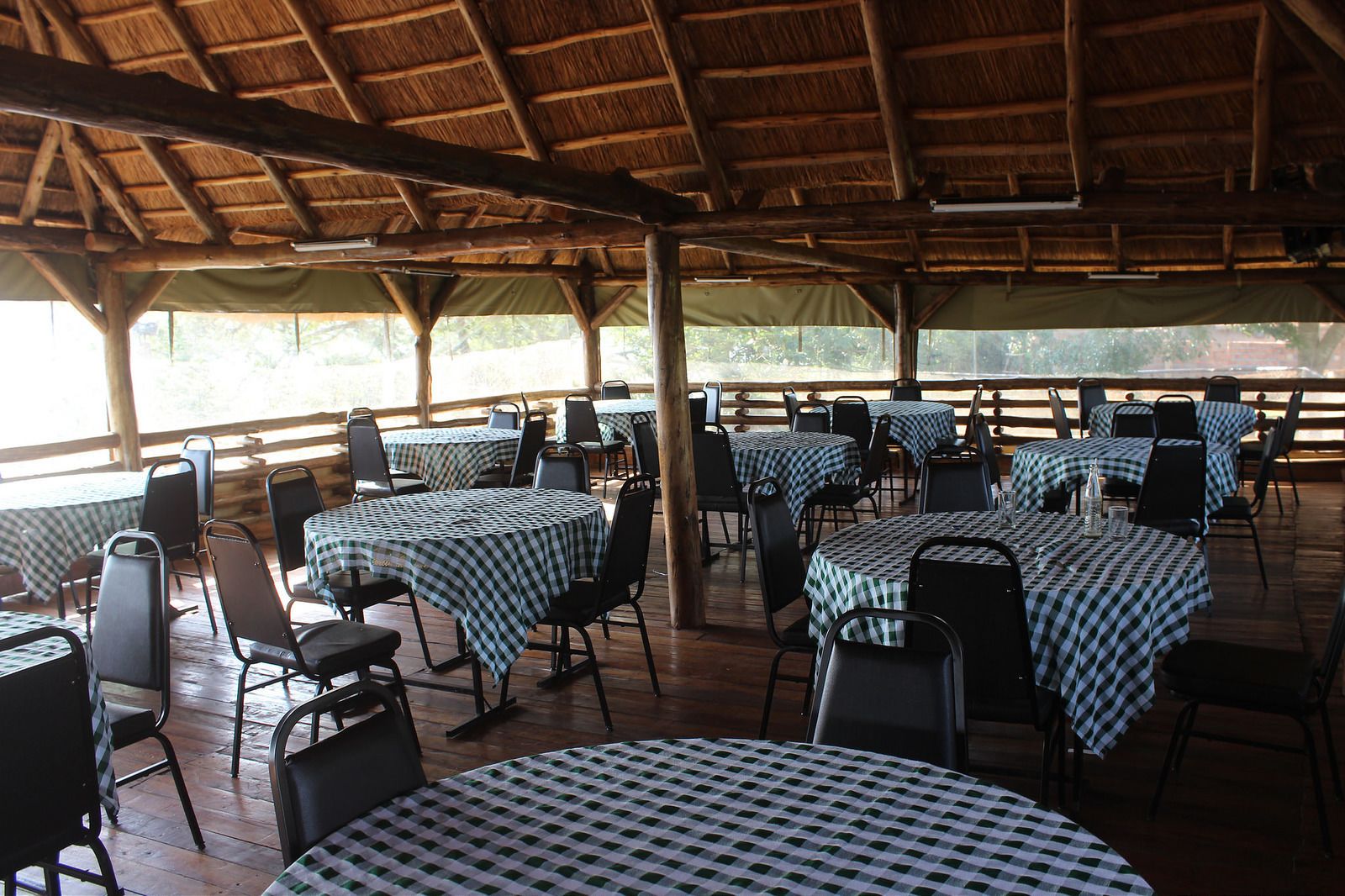 An outdoor dining area with tables and chairs, covered by a wooden roof, and surrounded by a wooden fence.