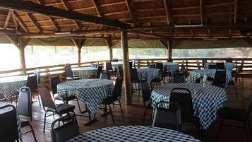 An outdoor dining area with tables and chairs, covered by a wooden roof, and surrounded by a wooden fence.