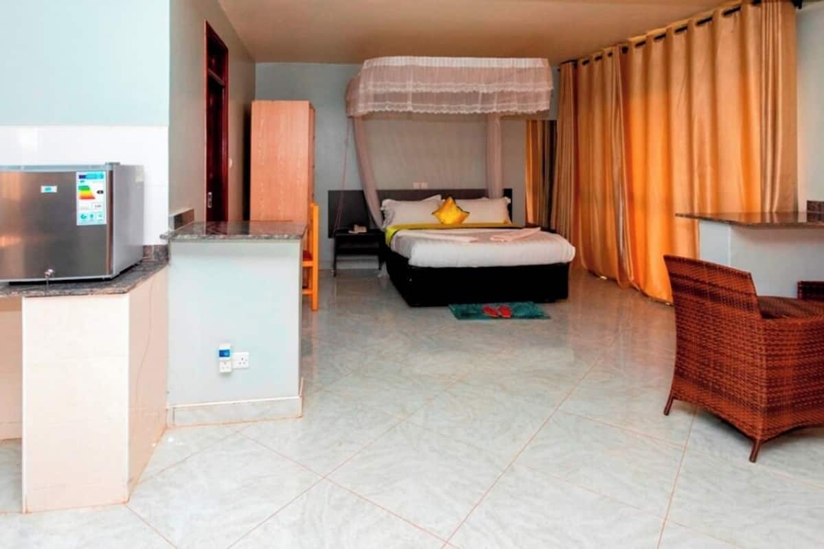 A hotel room with a bed, a desk, a refrigerator, and wicker chairs.