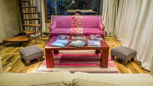 Ein gemütliches Wohnzimmer mit einem rosafarbenen Sofa, einem Holztisch mit Büchern und Blick auf Bäume durch ein Fenster.