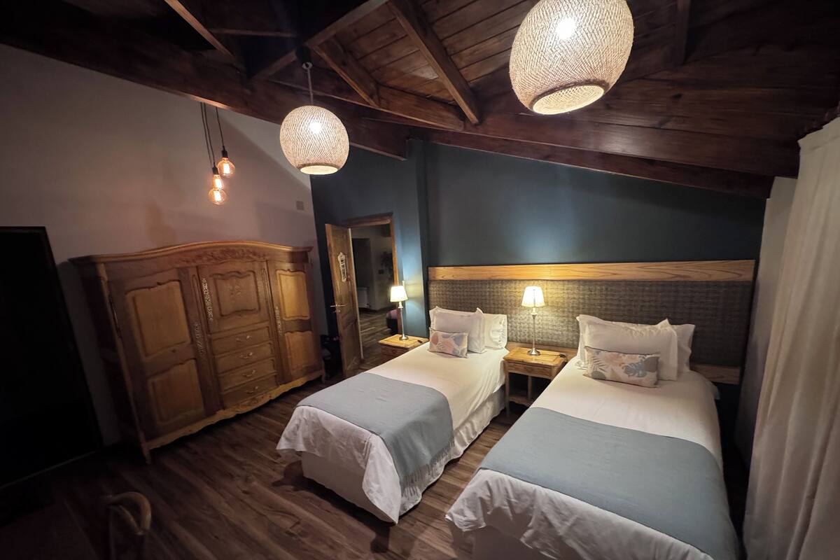 Una habitación con dos camas, un armario de madera e iluminación colgante.