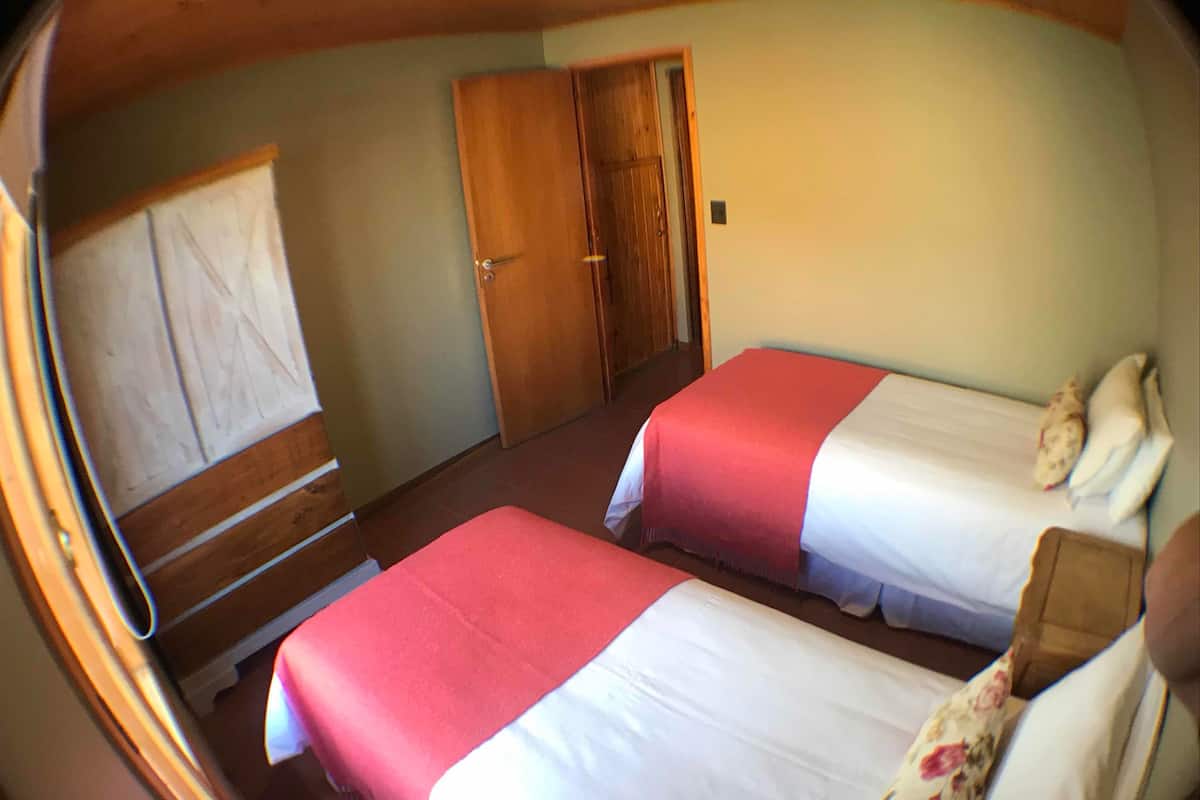 Una habitación con dos camas, una puerta de madera y una ventana con persianas.