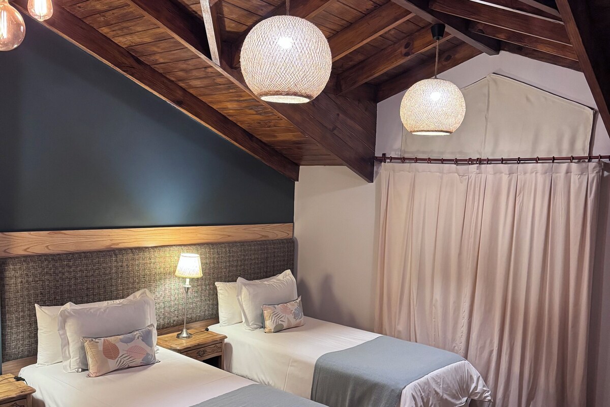 Une pièce chaleureuse avec deux lits, des poutres en bois au plafond et des luminaires tressés suspendus.