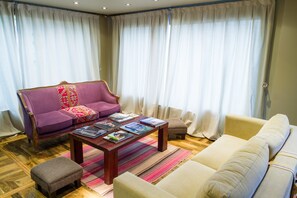 Ein Wohnzimmer mit einem violetten Sofa, einem beigefarbenen Sofa, einem Holztisch und einem Streifen Teppich.