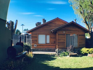 Eine Holzhütte mit Steinunterbau, einer kleinen Veranda und einem gepflegten Garten.