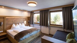 A modern hotel room with a wooden bed, a large window with curtains, a wooden bench, and a ceiling light.