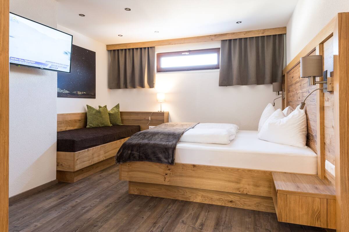 A bedroom with a wooden bed, a TV mounted on the wall, and a window with curtains.
