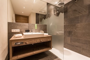 Un baño moderno con tocador de madera, un espejo grande y zona de ducha con mampara de vidrio.