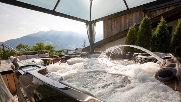 A hot tub with a wooden deck and a view of mountains.