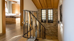 A staircase with a wooden finish and a stone wall with windows.