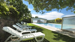 Un área junto a la piscina con sillones de descanso y una estructura de vidrio.