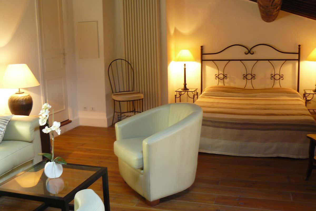 A bedroom with a bed, a chair, a table, and two lamps.