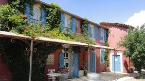 Un edificio con fachada roja, contraventanas azules y una zona de estar exterior cubierta con una mesa y sillas de metal.