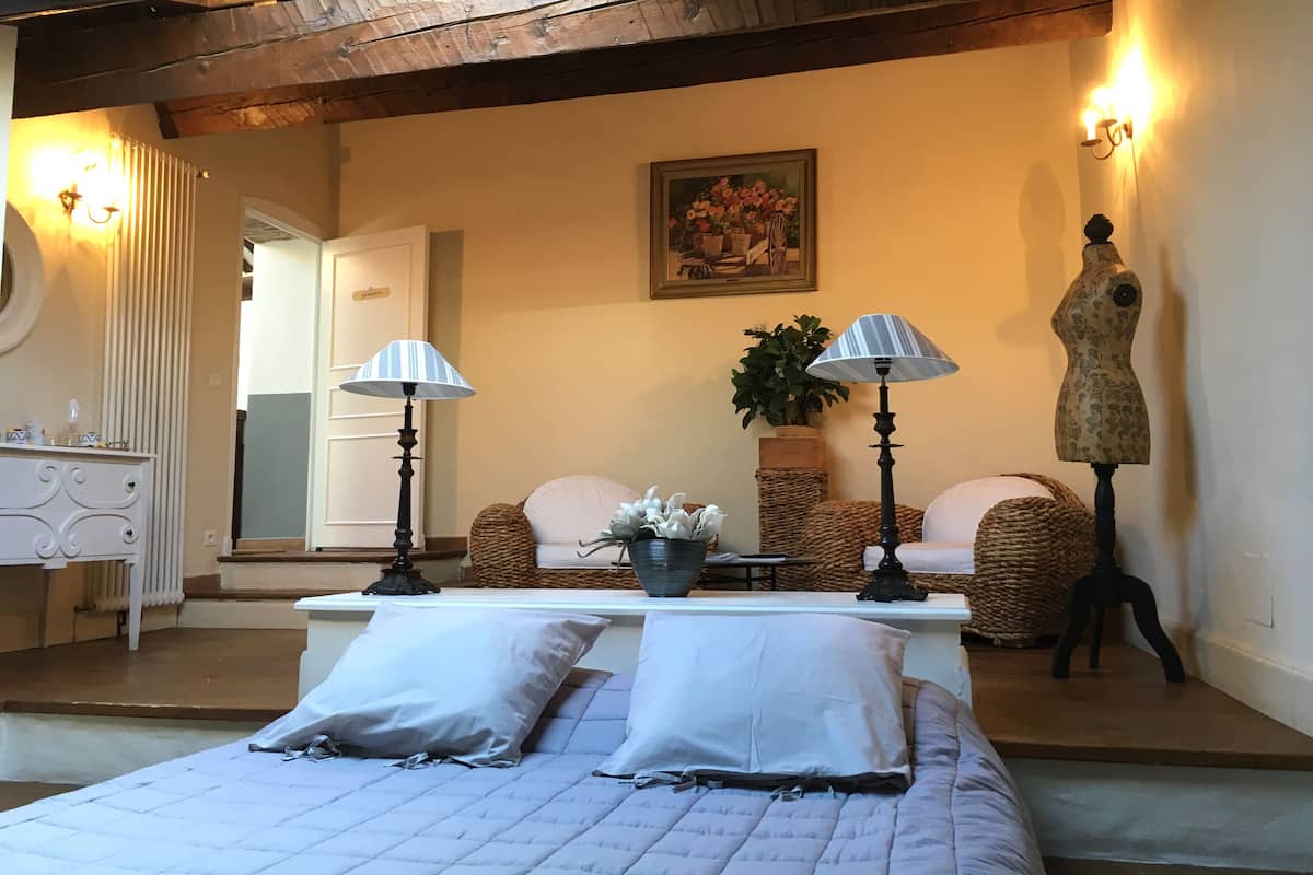 A bedroom with a bed, two bedside lamps, a dresser, a mirror, a potted plant, a mannequin, and a painting on the wall.