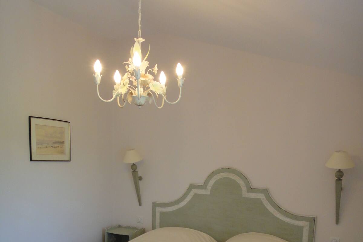 A double bed with a metal frame, two bedside tables, a chandelier, and a framed picture on the wall.