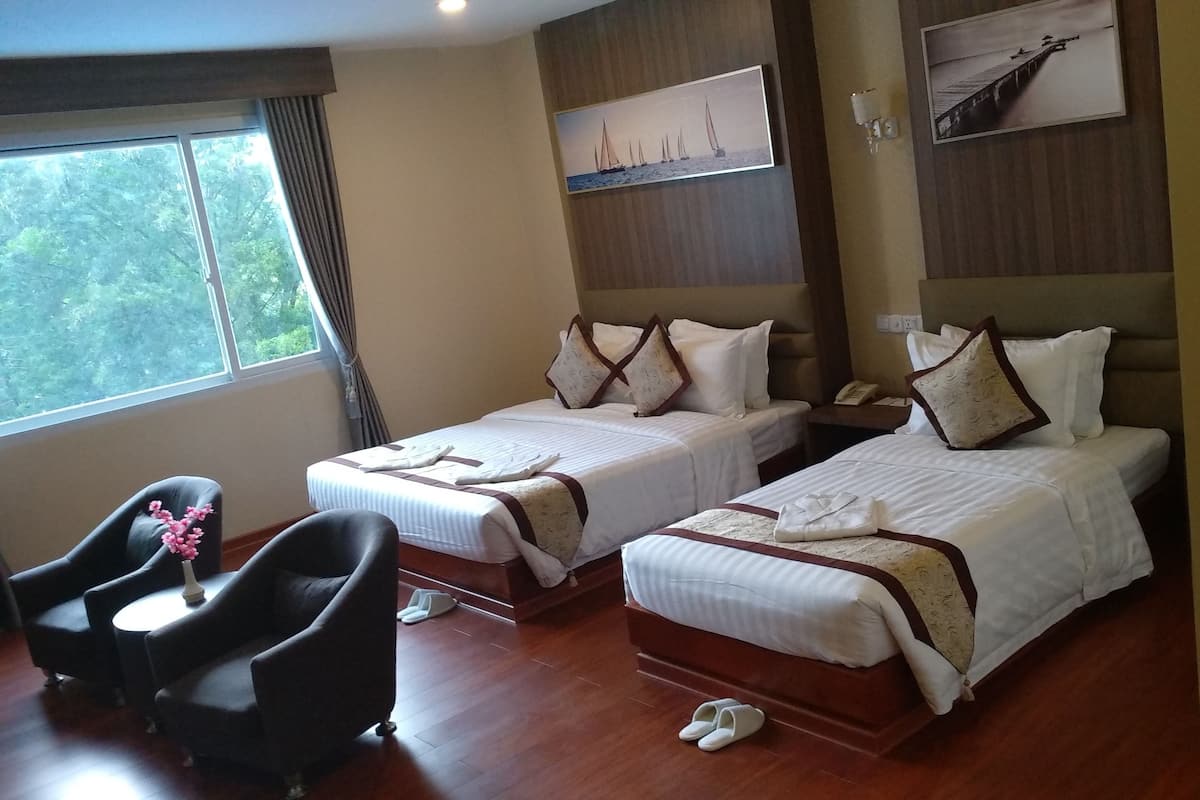 Une chambre d’hôtel avec deux lits, un bureau, une chaise et une fenêtre donnant sur des arbres.