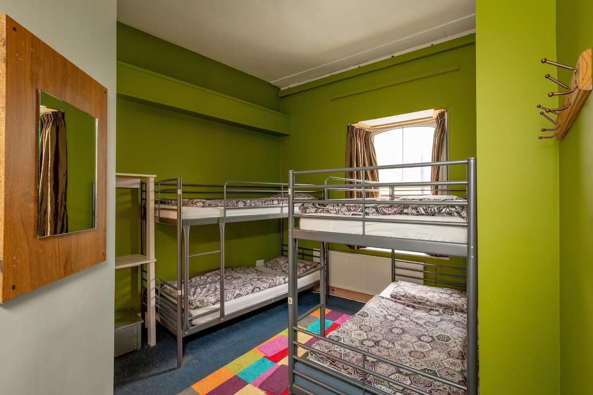 Ein Zimmer mit Etagenbetten, einem fenster mit Vorhängen, einem Spiegel und einem farbenfrohen Teppich.
