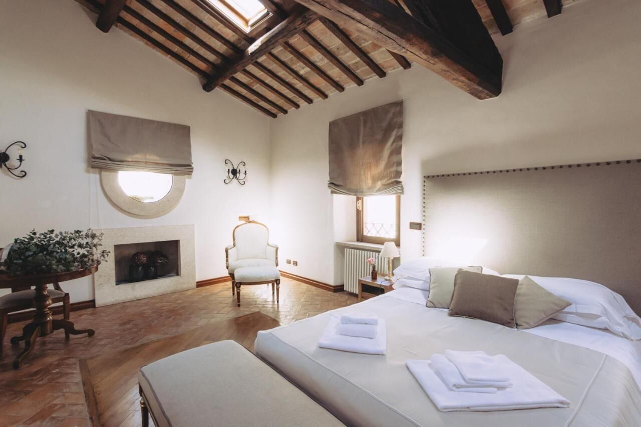 A bedroom with a large bed, a fireplace, a chair, and a table with a plant.