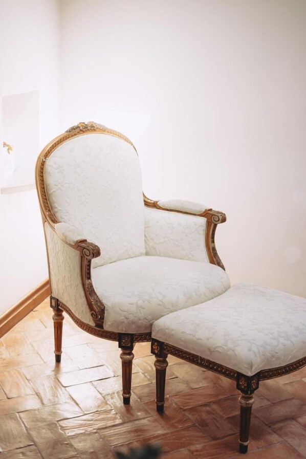 A chair with a high back and armrests, upholstered in a light fabric, positioned on a wooden floor.