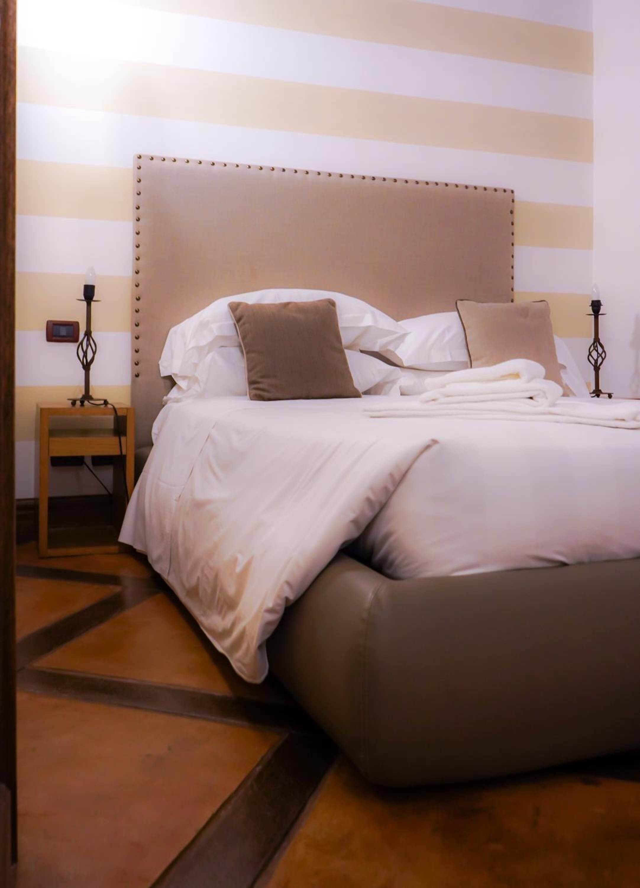 Una cama bien hecha con cabecera, una mesita de noche con lámpara y una pared con rayas horizontales.