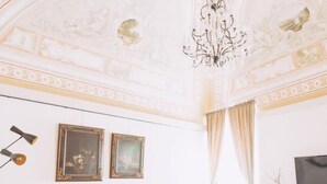 A room with a brown sofa, a white armchair, a coffee table, and a TV on a wooden cabinet. - Al Palazzetto B&B (Tivoli)