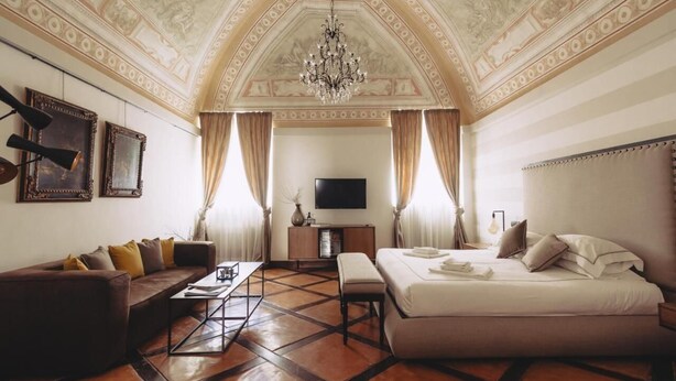 A spacious room with a large bed, a sofa, a television, and a chandelier. - Al Palazzetto B&B (Tivoli)