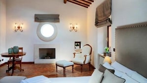 A cozy room with a fireplace, a round skylight, a bed, a dining table, and two chairs. - Al Palazzetto B&B (Tivoli)