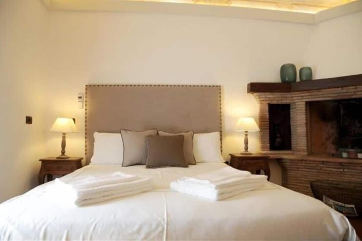 A neatly made bed with folded towels, two bedside lamps, and a fireplace.