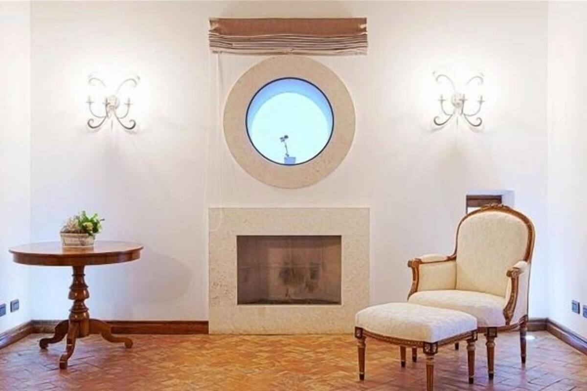 A room with a fireplace, a round window, a chair, and a table.
