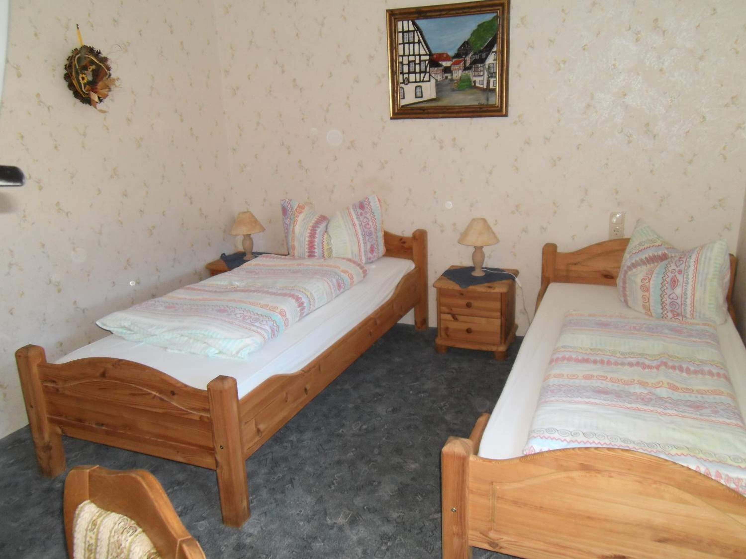 Ein Schlafzimmer mit zwei Holzbett, einem Nachttisch, einem Sessel und einem an der Wand hängenden Gemälde.