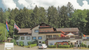 A hotel with a balcony, a sign indicating it is open, and a van parked in front.