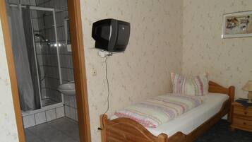 Ein kleines Schlafzimmer mit einem hölzernen Bett, einem an der Wand montierten Fernseher, einer Duschkabine und einer Toilette.