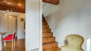 Un escalier avec des marches en bois, une chaise rouge et un fauteuil vert à revêtement en tissu, dans une pièce dont le sol est en bois et les murs sont blancs.