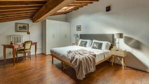 Une chambre avec un plafond en bois, un lit avec des oreillers, une table de chevet, une chaise et un radiateur.