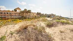 Ein Hotel an der Küste mit mehreren Balkonen, einem Sandstrand und Palmen.